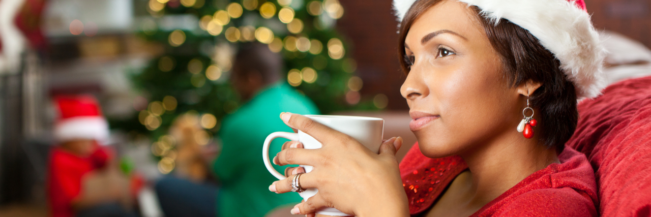 woman drinking from a mug next to the christmas tree