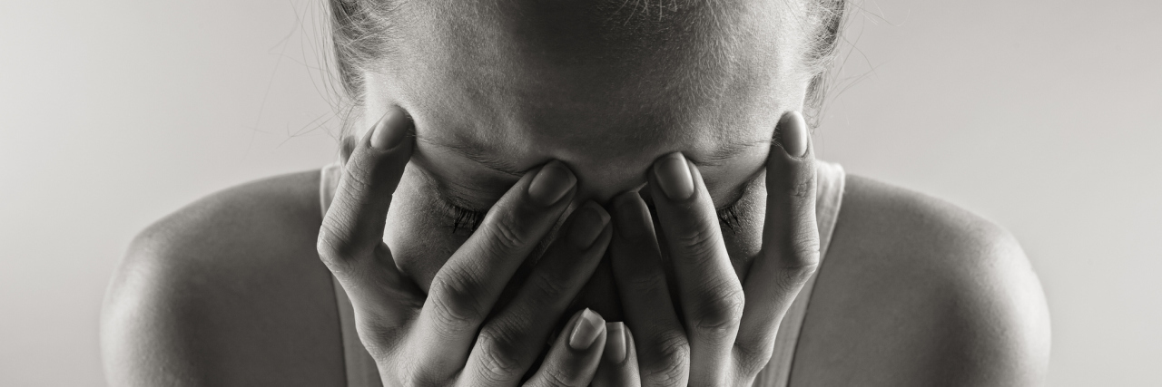 When I Wonder Who I Would Be Without POTS A black and white photo of a woman crying into her hands.