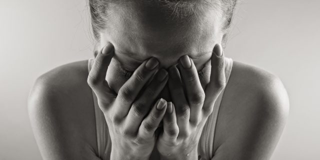 A black and white photo of a woman crying into her hands.