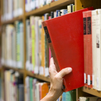 A hand picks out a book from a row of books on a shelf.