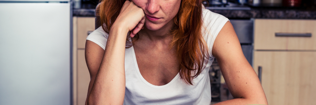 What It's Like to Take Medical Leave Due to Rheumatoid Arthritis woman sitting at kitchen table with her head resting on her hand