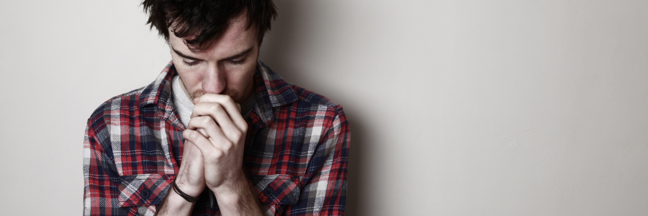 How My Thoughts of Suicide Strengthened My Empathy As a Therapist worried young man against plain wall looking down with hands closed