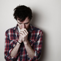worried young man against plain wall looking down with hands closed