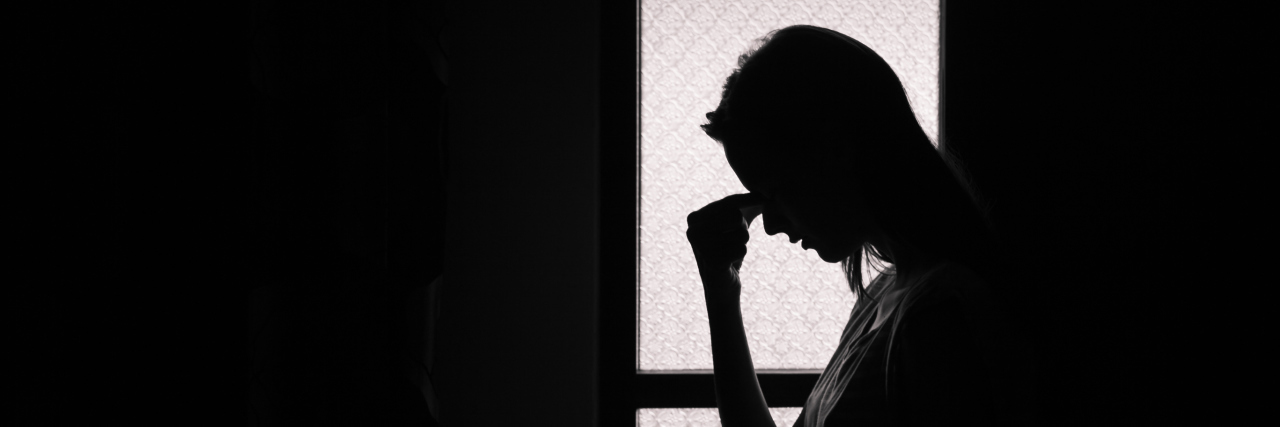 The Importance of Using Proper Syntax to Talk About Migraine silhouette of a woman holding her head in a dark room