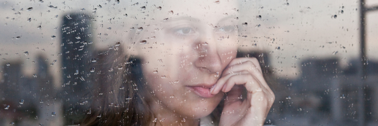 young woman looking anxious out of rainy window