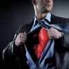 businessman opening shirt to reveal red superhero costume underneath superman pose