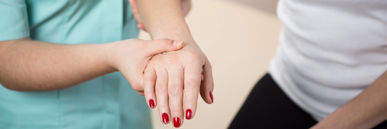 A close-up image of a physical therapist helping a patient, holding her arm and hand.
