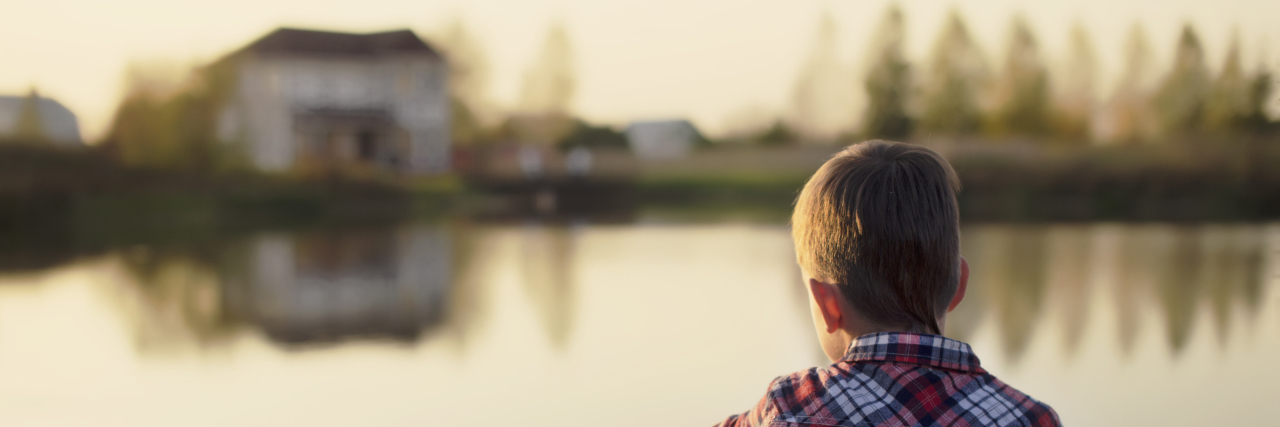 When Your Child's Rare Disease Journey Starts to Affect Them Mentally child dreaming sitting on a wooden pier near the water and looking at the house and the people on the other side