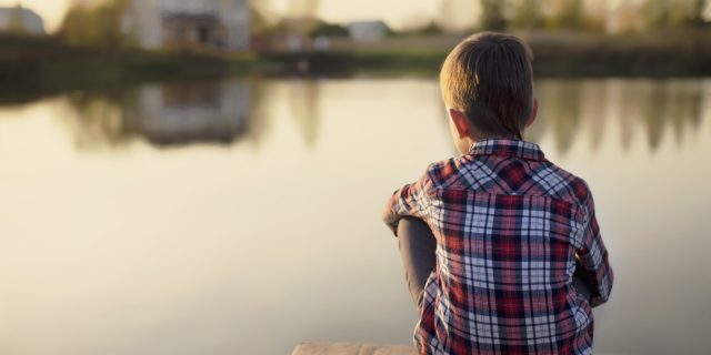 When Your Child's Rare Disease Journey Starts to Affect Them Mentally child dreaming sitting on a wooden pier near the water and looking at the house and the people on the other side