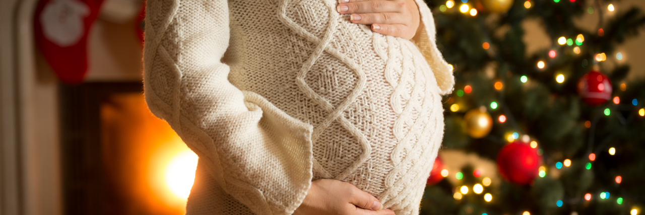 This Holiday Season, Please Don’t Drink While Pregnant Pregnant woman posing against fireplace and Christmas tree.