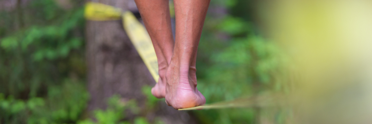 Striving for Balance in the New Year With Chronic Illness woman balancing on a slack line in the forest