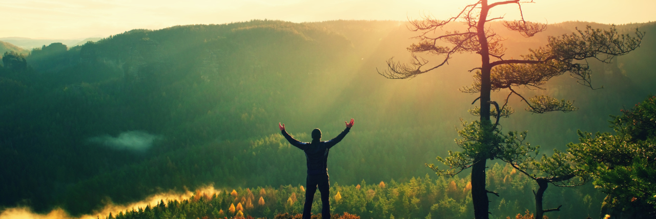 Cerebral Palsy Taught Me to Fall, Not Fail Hiker with hands in the air stands on a misty hill.