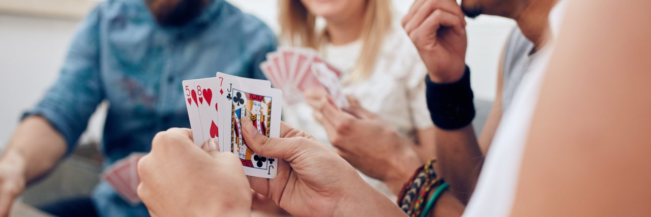 Group of friends sitting together playing cards. Focus on playing cards in hands of a woman during a party.