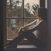 A woman siting on a window sill, looking outside.