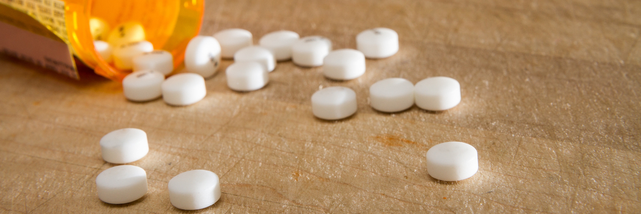 When My Opioid Medication Was Taken Off the Market White pills spread across a white table, falling out of the medication bottle.