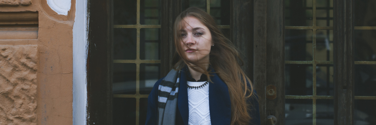 What to Know About People With Chronic Pain woman in coat and scarf standing outside a door
