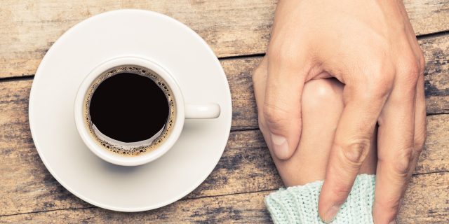 close up of people holding hands on table beside cup of coffee