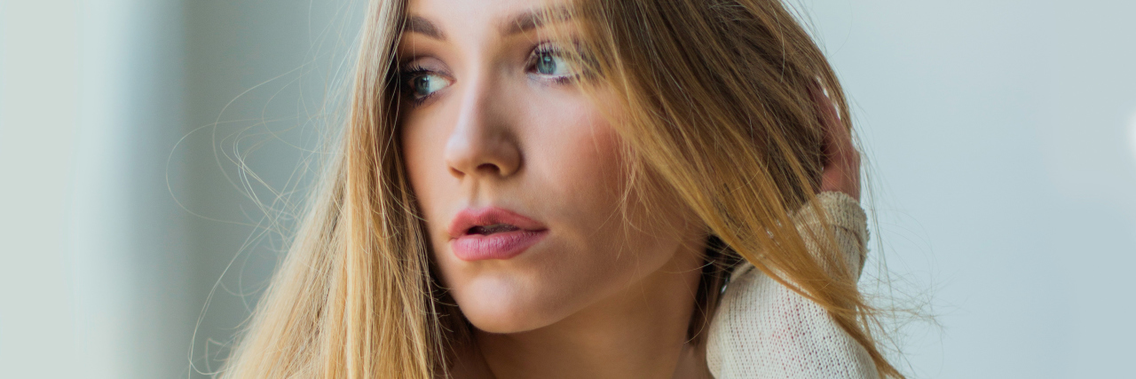 When You Wonder If Full Eating Disorder Recovery Is Possible Young blonde woman sitting next to window in sweater, looking emotive and thoughtful