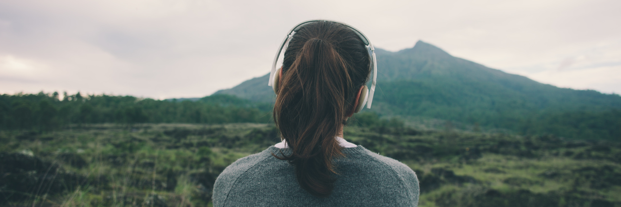 11 Songs That Help Me Maintain Resilience Against Mental Illness Woman in headphones listening music in nature and at the mountain (intentional pale color style)