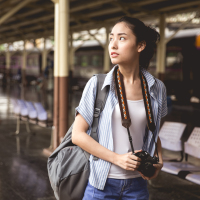 young asian woman holding a camera and backpack