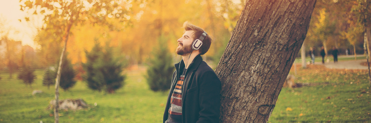 Why I Stopped Explaining My Brain Injury Man with headphones leaning on a tree in park.