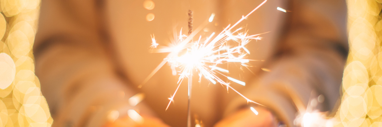 New Year's Resolutions I'm Setting Because of My Illnesses A woman holding a sparkler.