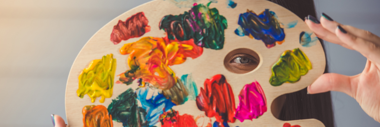 Fibromyalgia Affecting Artist's Creativity A woman holding an art easel to her face, which has paint on it.