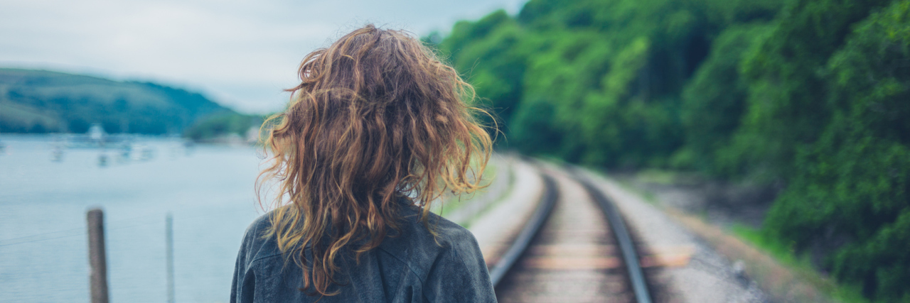 What to Know When You're Diagnosed With Chronic Illness woman walking on railroad tracks next to a lake