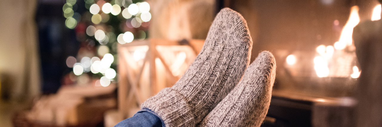 Why I'm Not Looking Forward to Christmas With Chronic Illness a person wearing socks in front of the fireplace and a christmas tree