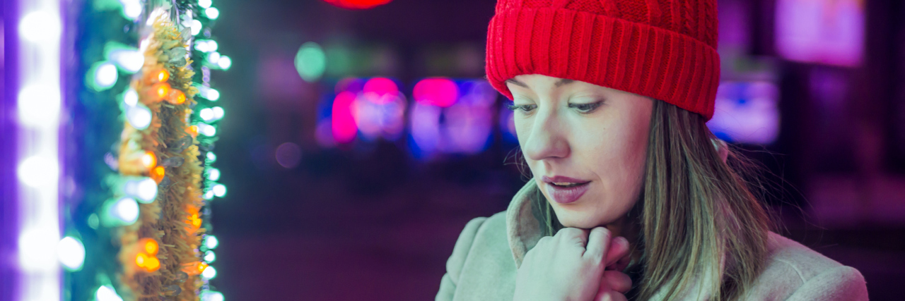 How to Get Through the Holidays With Depression young woman standing by christmas tree outdoors wearin hat and gloves