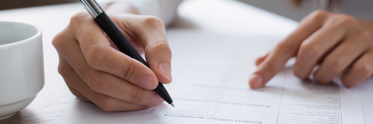 Woman holding pen and filling out application form at table.