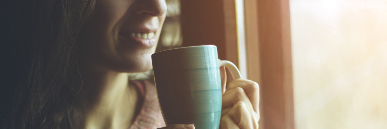 What I'm Thinking About on the New Year With Chronic Illness woman sitting next to a window drinking coffee during winter