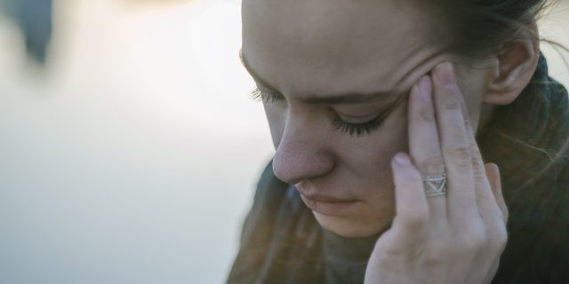 A young woman holding her hand to her temple, looking like she's tired and/or in pain.