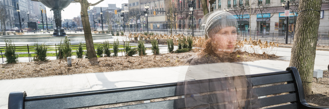 A young woman sits on a downtown city bench feeling invisible feeling the unseen difficulty of mental illness