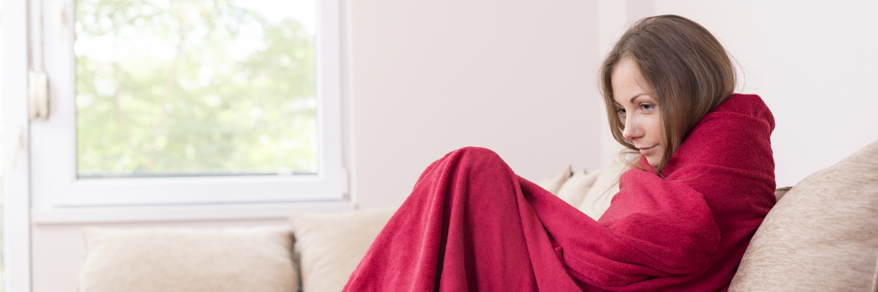 How I Grieve During the Holidays, 5 Minutes at a Time Young woman sitting on a couch covered with blanket, having a fever.
