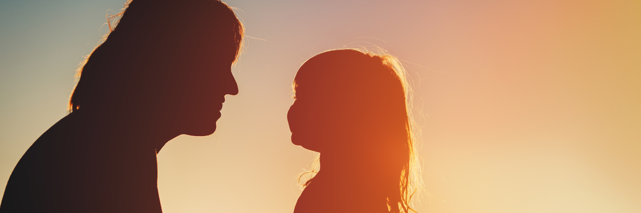 Silhouette of happy mother and little daughter at sunset.