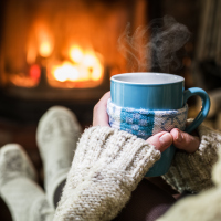 woman sitting with a mug and a blanket in front of the fire