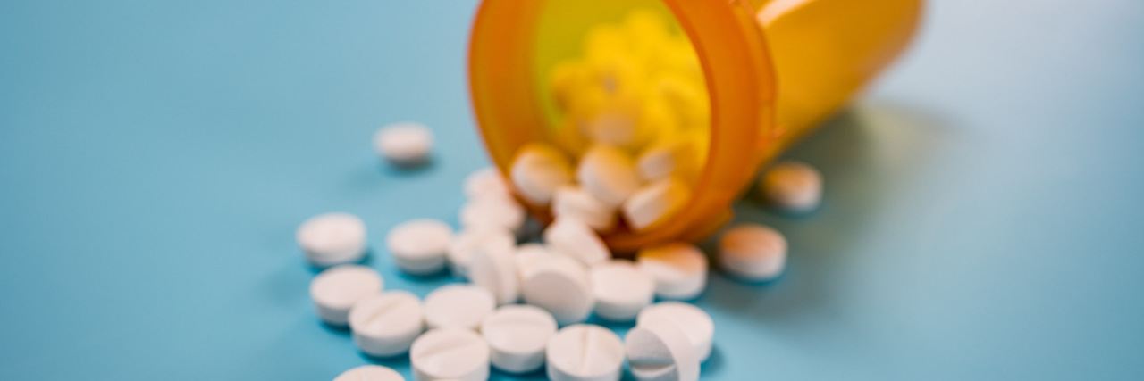 Fighting the Stigma Against Chronic Pain Patients Who Use Opioids white pills spilling out of container on blue table