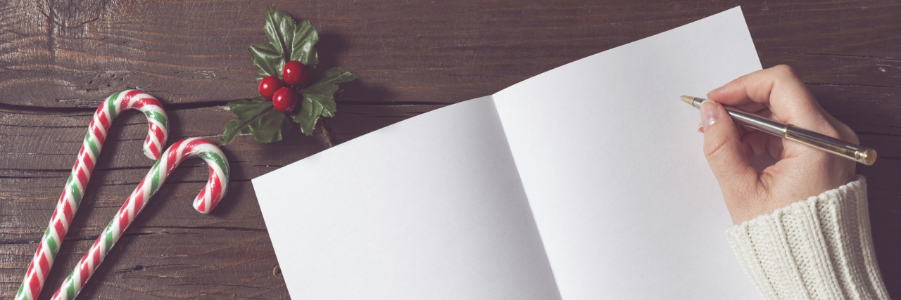 Writing Christmas Cards With Fibromyalgia Brain Fog A woman writing Christmas cards, with Christmas decor around her on the table.