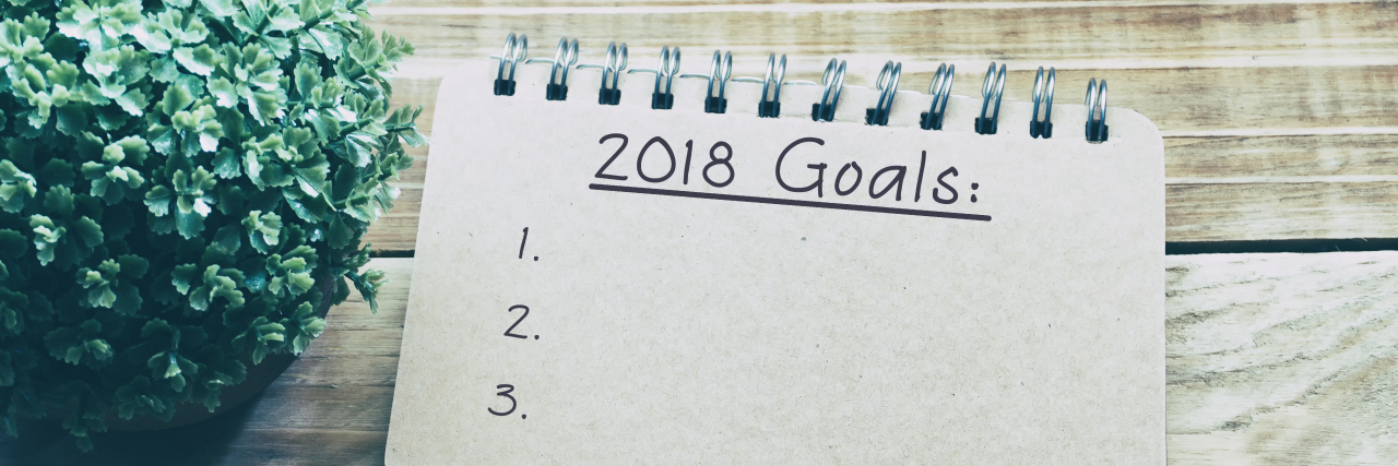 picture of a notebook and pen. on the paper "2018 goals" is written.
