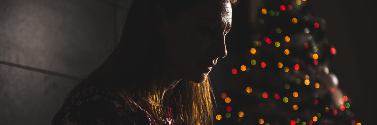 woman sitting next to a christmas tree in the dark looking upset