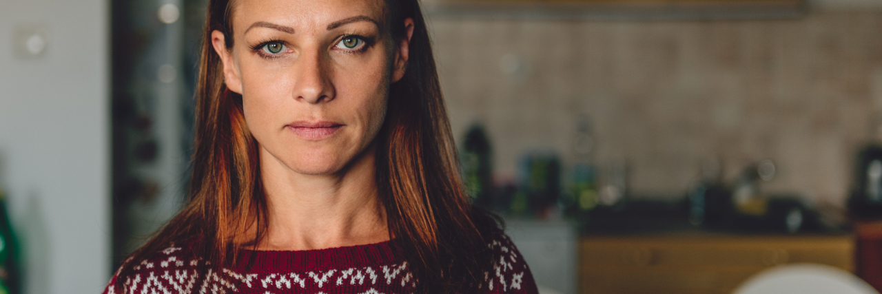 I Feel Obligated to Attend Holiday Parties but Have Social Anxiety Portrait of woman standing in front of the kitchen wearing red sweater with christmas motifs