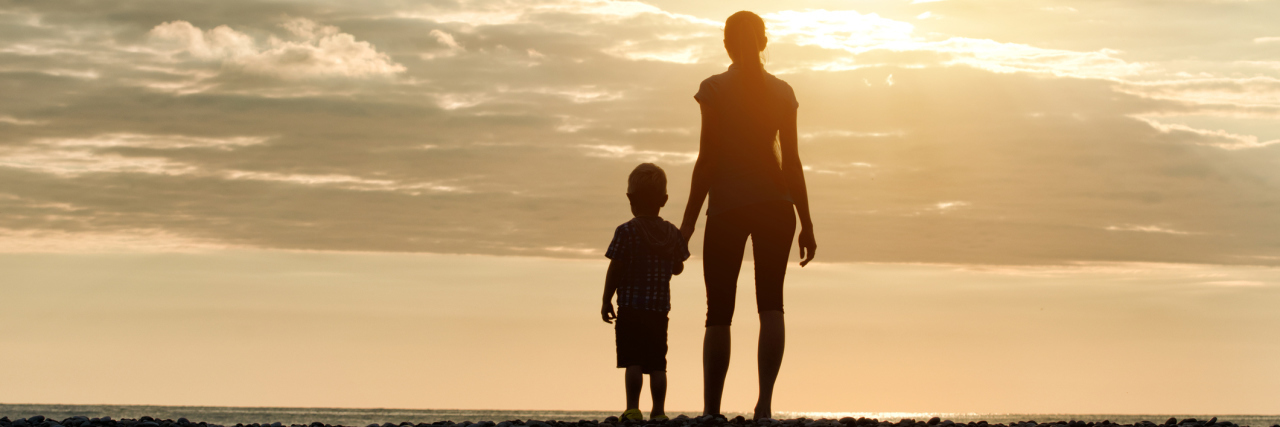 silhouettes of mother and son standing on beach
