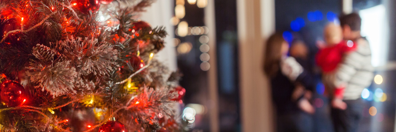 Christmas scene with happy family of four, tree gifts and window in blurred bokeh background, copy space