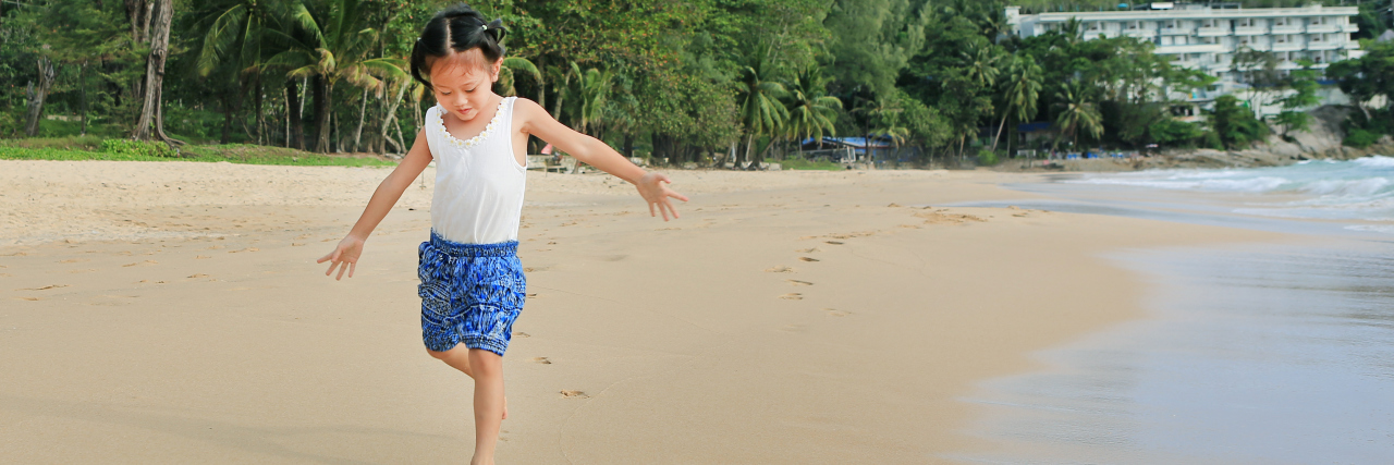 Little Asian girl running on the beach.