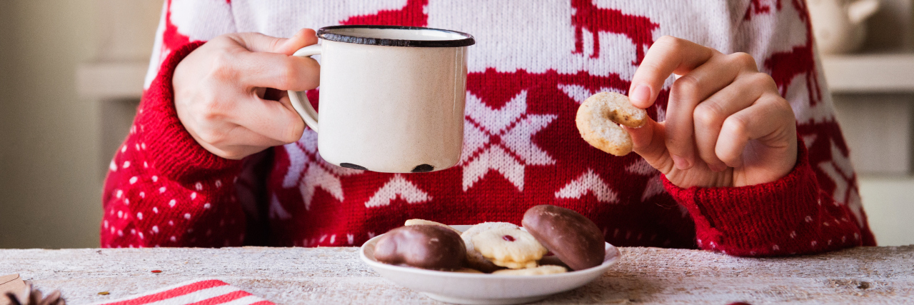 Navigating the Holidays With Ankylosing Spondylitis woman wearing a christmas sweater and holding a mug and a cookie