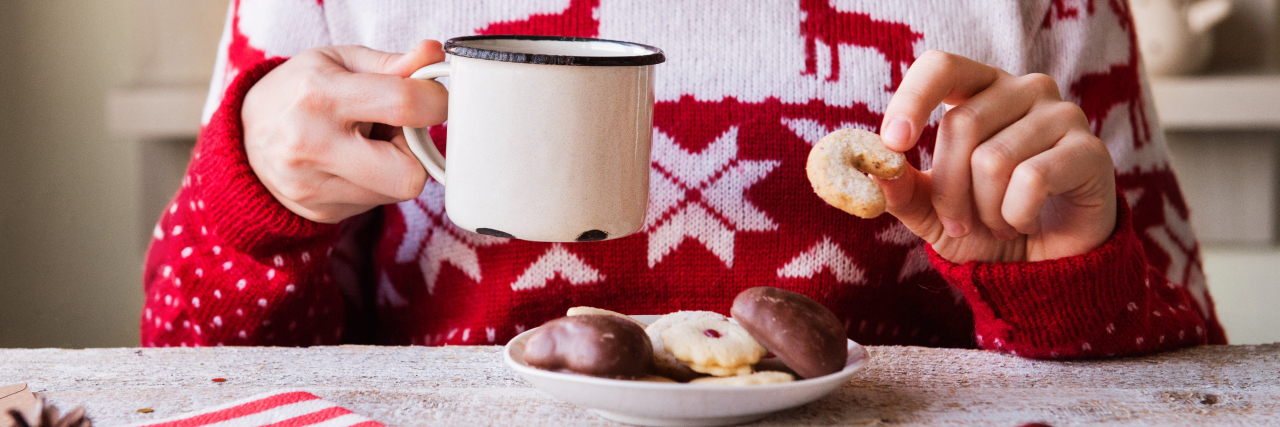 woman wearing a christmas sweater and holding a mug and a cookie