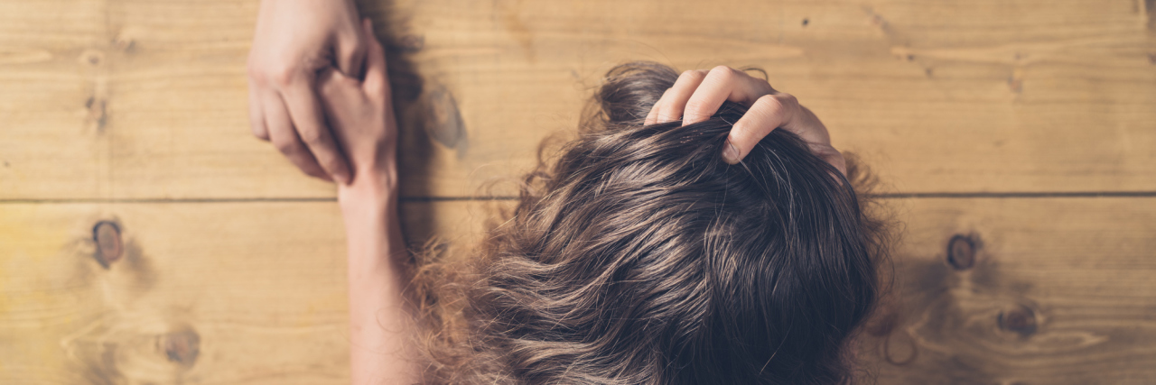 When Relationships End Because of Chronic Illness An upset woman at a wooden table, with a man holding her hand.