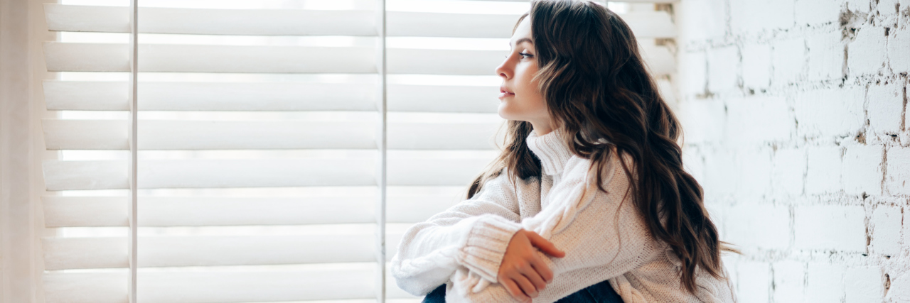 What to Expect From Christmas When You Have a Mental Illness young woman at home sitting by window at christmas