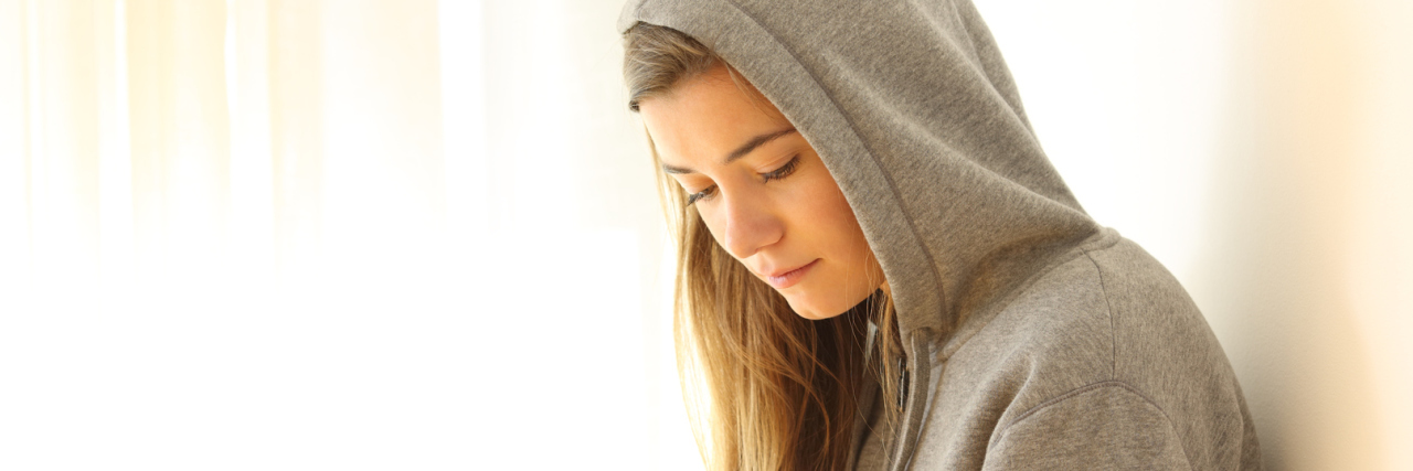 The Unbelievable Way My Allergy Doctor Stigmatized My Mental Illness pensive teen looking down indoors wearing a white hoodie